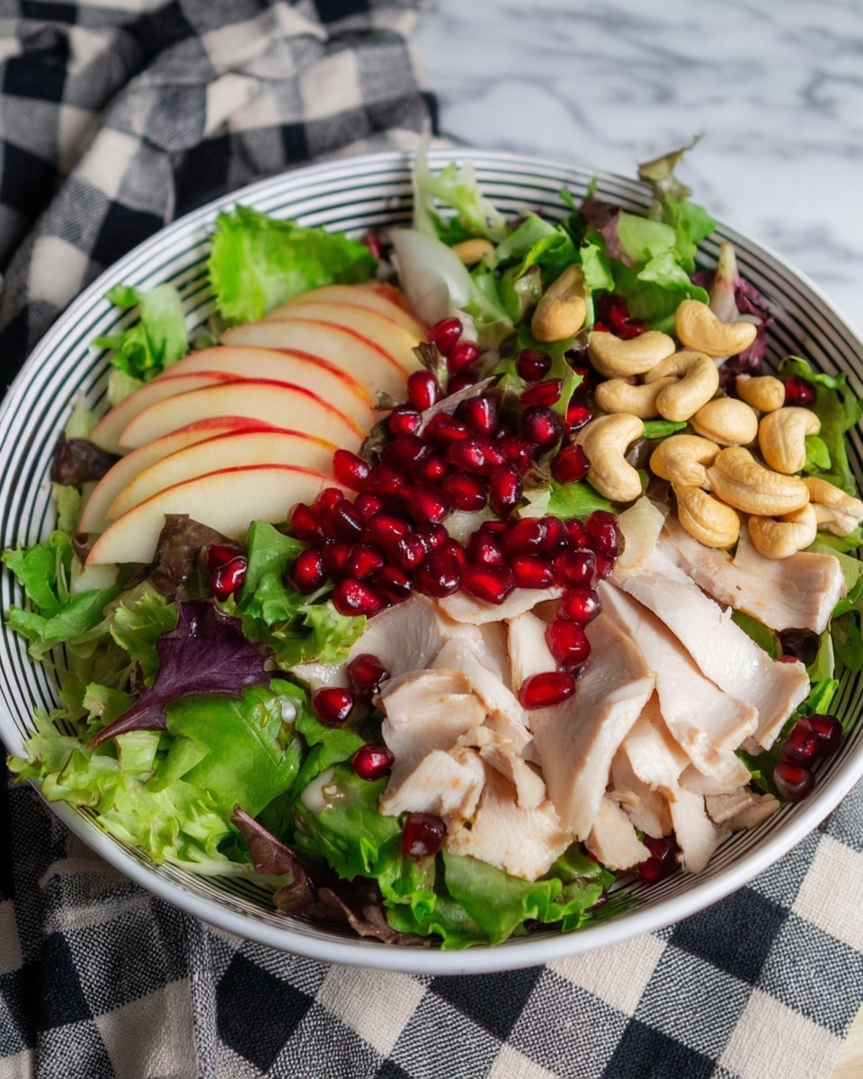 A fresh salad is shown in a white bowl with black lines on the outside. The bottom layer has mixed green leaves with bright and dark green colors and some purple-red leaves scattered in. On the left side, thin apple slices with red and yellow skin are layered upright. On top of the leaves, there are light beige turkey slices spread out in the middle. Bright red pomegranate seeds are sprinkled over the turkey slices, adding a shiny texture. On the right side, light brown cashew nuts are placed on top of the greens. The bowl is placed on a white marbled surface with part of a black and white checkered cloth visible in the background. photo taken with an iphone --ar 4:5 --v 7