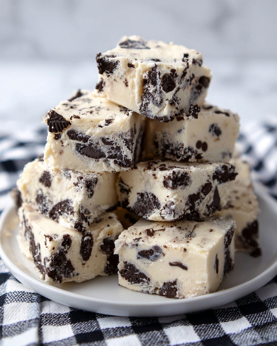 A pile of seven square-shaped cookies and cream fudge pieces stacked on a white plate, each piece showing a mix of creamy pale beige fudge with uneven chunks of dark chocolate cookie pieces scattered throughout. The fudge has a smooth, slightly shiny texture with rough edges where the squares were cut. The plate sits on a cloth with a black and white checkered pattern, all placed on a white marbled surface. photo taken with an iphone --ar 4:5 --v 7