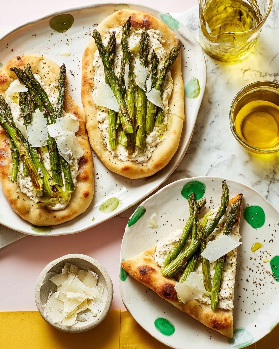 Two oval flatbreads are shown on a white plate with green speckles, each topped with a creamy white base, several long green asparagus stalks arranged lengthwise, and sprinkled with thin shavings of pale yellow cheese. One flatbread has some browned spots on the dough's light golden crust, giving a slightly crispy texture. Next to this, a white plate holds two triangular slices of a similar flatbread with the same toppings, showing fluffy dough edges and scattered cheese shavings. Surrounding the plates on a white marbled surface are a small ceramic bowl of cheese shavings, a glass jug of golden oil, and a small dish of black pepper. photo taken with an iphone --ar 4:5 --v 7