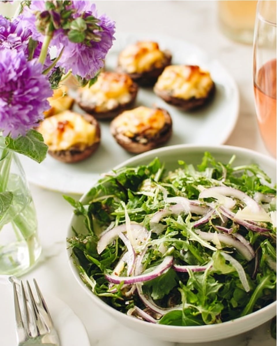 The image shows a close-up of a fresh green salad in the front with thinly sliced white onions and purple onion slices mixed with leafy greens. Behind it, there is a white plate holding several stuffed mushrooms topped with melted cheese, baked to a golden brown. The setting is on a white marbled surface and a small vase with purple flowers is visible on the left side. A glass containing a light-colored drink is on the right side of the frame. Photo taken with an iphone --ar 4:5 --v 7