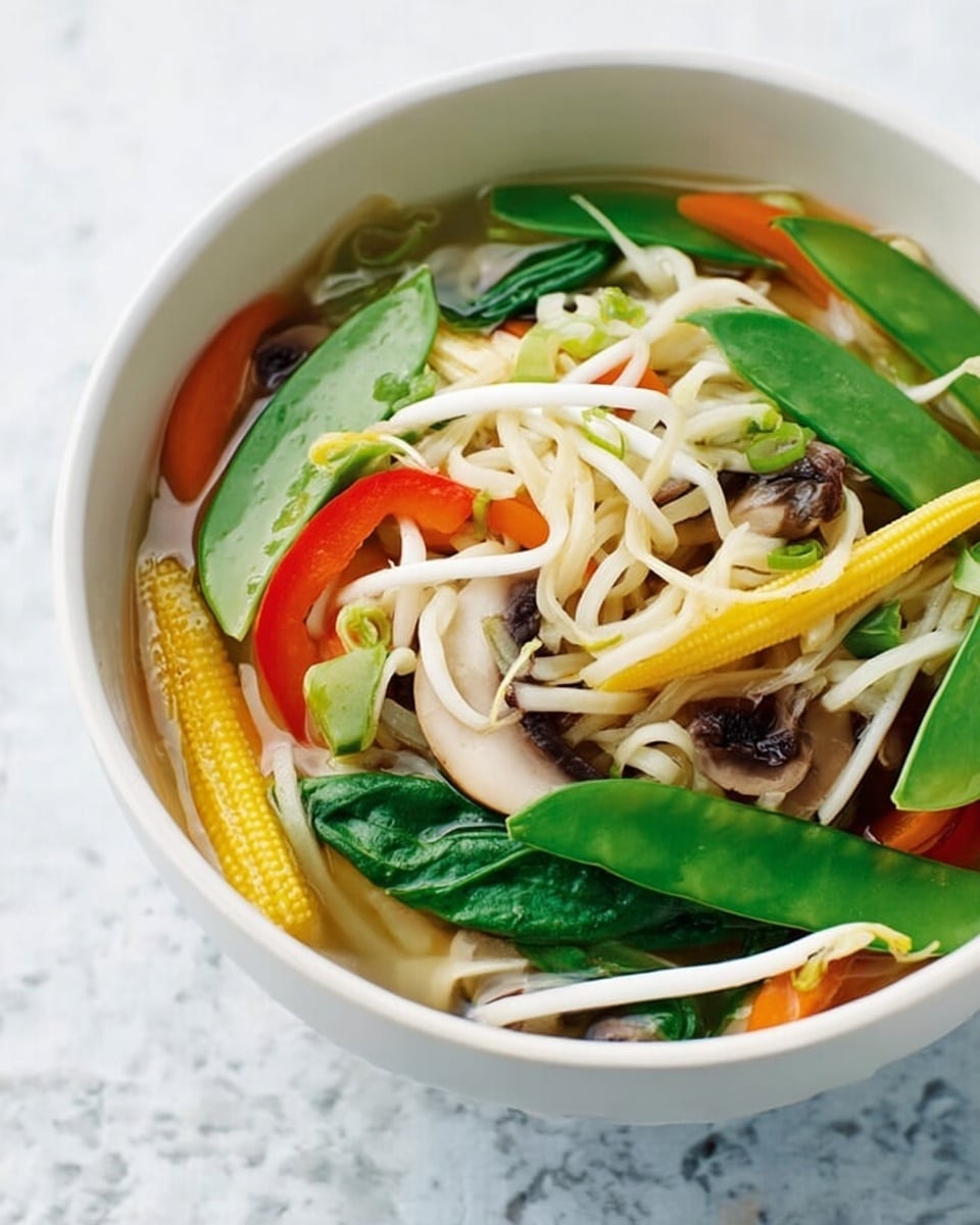 A white bowl filled with a colorful vegetable noodle soup sits on a white marbled surface. The soup has three visible layers: the bottom layer is clear broth, slightly shiny and smooth; the middle layer holds light beige noodles that look soft and slightly twisted; the top layer is a mix of bright vegetables including dark green leafy spinach, pale yellow baby corn, thin red and orange carrot strips, green snap peas, and light-colored bean sprouts, all creating a fresh, textured look. photo taken with an iphone --ar 4:5 --v 7