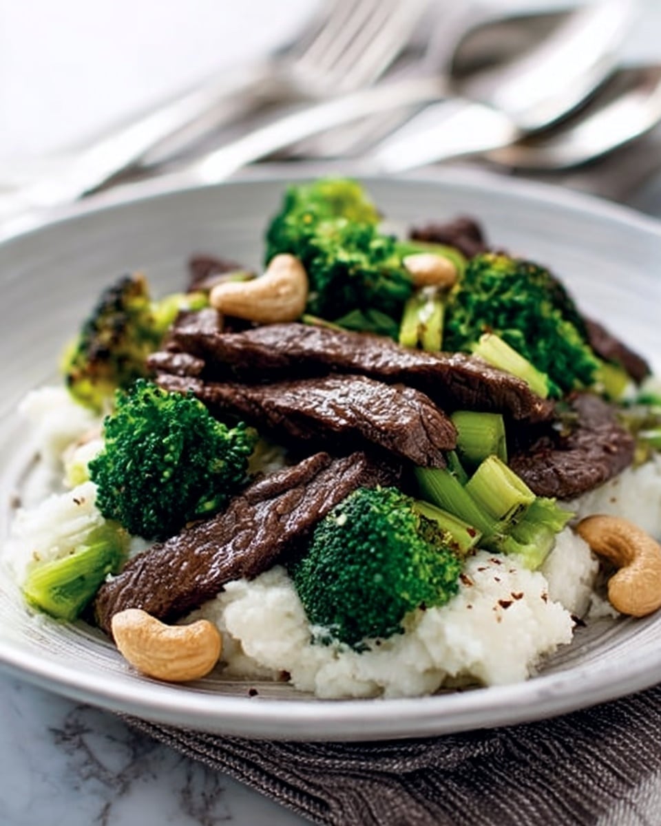 The image shows a white plate with a serving of food made of several parts. On the bottom is a pile of white rice, soft and fluffy, positioned at the back. In front of the rice are medium-sized pieces of dark brown cooked beef strips, placed randomly but layered across the plate. Bright green broccoli florets and sliced celery are scattered among the beef, adding a fresh and vibrant touch. Light golden roasted cashew nuts are spread evenly on top and around the meat and vegetables. To the right side of the plate is a small portion of creamy white sauce with a smooth texture. The plate sits on a white marbled surface with soft natural lighting, showing the colors and textures clearly. Photo taken with an iphone --ar 4:5 --v 7