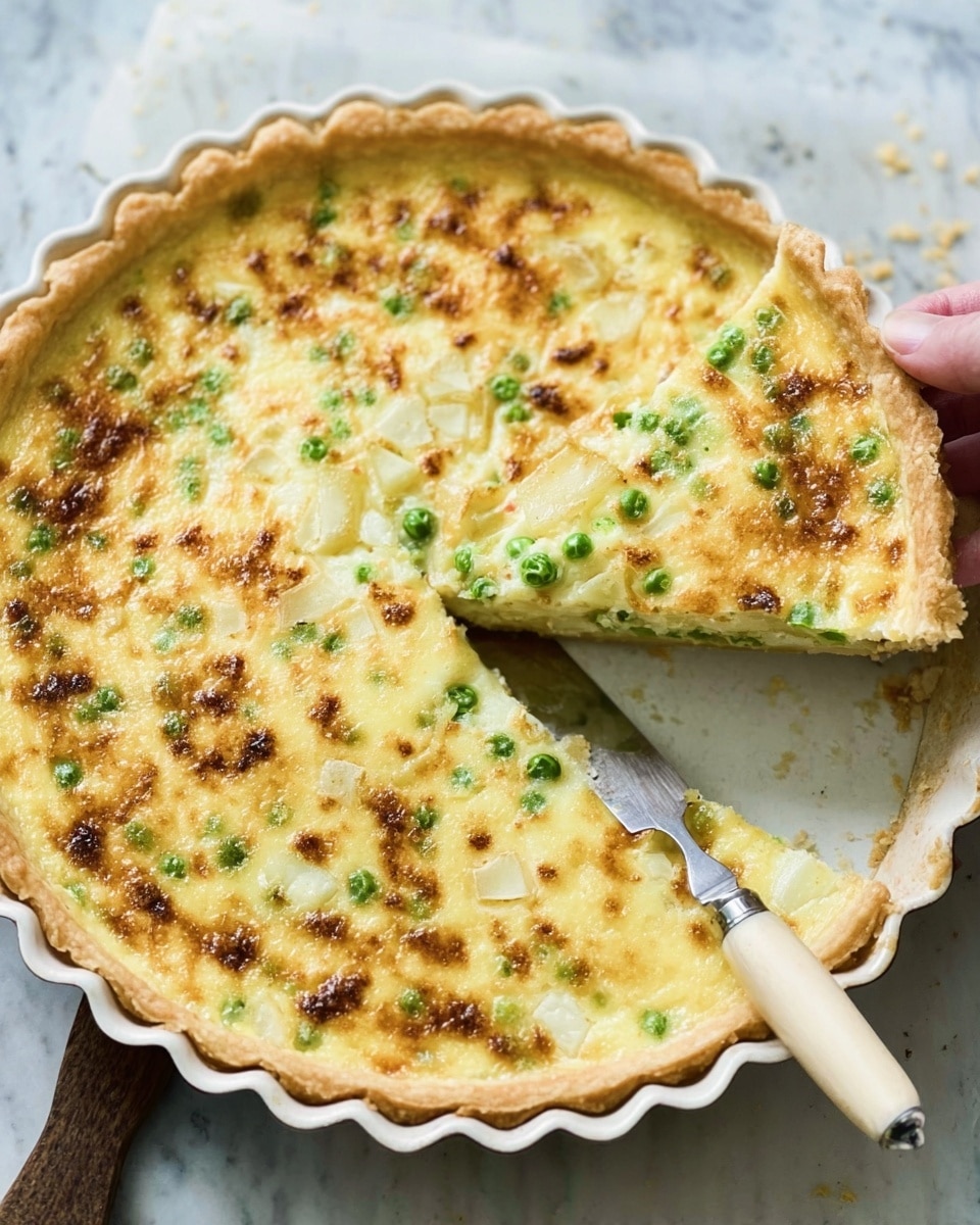 The image shows a golden-brown quiche in a round tart pan with scalloped edges, with one slice being lifted out revealing a smooth, creamy inside layer. The top layer is slightly browned with small green pieces evenly spread throughout, likely chopped green onions or herbs. The filling looks soft and creamy with visible chunks of a pale yellow ingredient, possibly potatoes. A knife with a wooden handle rests inside the pan. The background is a white marbled texture. photo taken with an iphone --ar 4:5 --v 7
