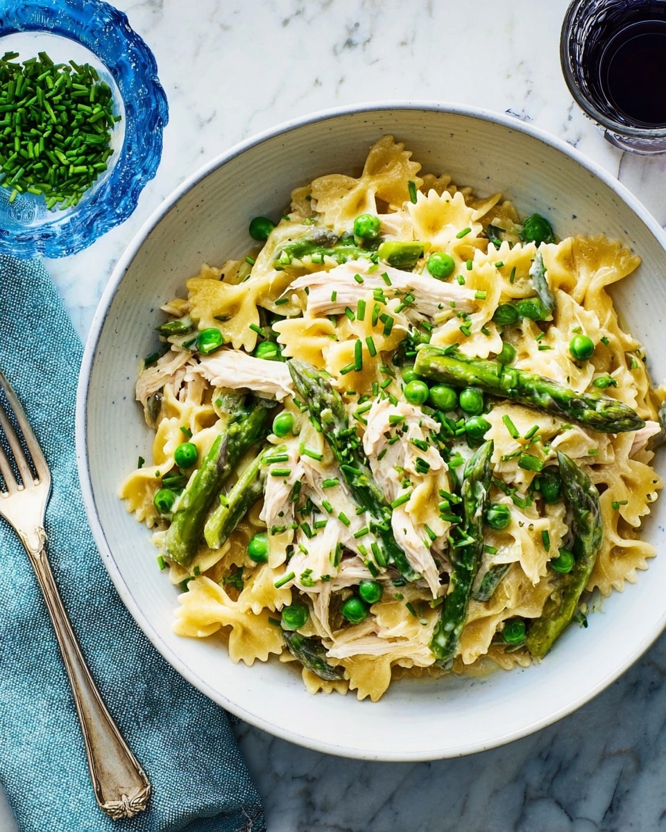 A white bowl filled with creamy pasta as the base layer, featuring farfalle pasta coated in a light yellow sauce; scattered on top are pieces of white chicken meat, bright green peas, and spears of asparagus adding texture and color; finely chopped green chives sprinkled over the whole dish to finish, giving a fresh, vibrant look; the bowl sits on a white marbled surface, next to a silver fork on a pale blue napkin, with a small glass of a dark drink nearby. photo taken with an iphone --ar 4:5 --v 7