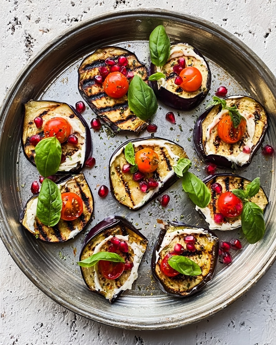 The image shows a round, shallow, silver plate on a white marbled surface. On the plate, there are eight small pieces of grilled eggplant, each about one layer thick with dark grill marks and a slightly wrinkled texture. Each eggplant piece is topped with a creamy white sauce layer, a green spinach or basil leaf, half of a bright orange cherry tomato, and scattered red pomegranate seeds. The colors include dark purple from the eggplant edges, white from the sauce, green from the leaves, orange from the tomatoes, and red from the pomegranate seeds. Photo taken with an iphone --ar 4:5 --v 7