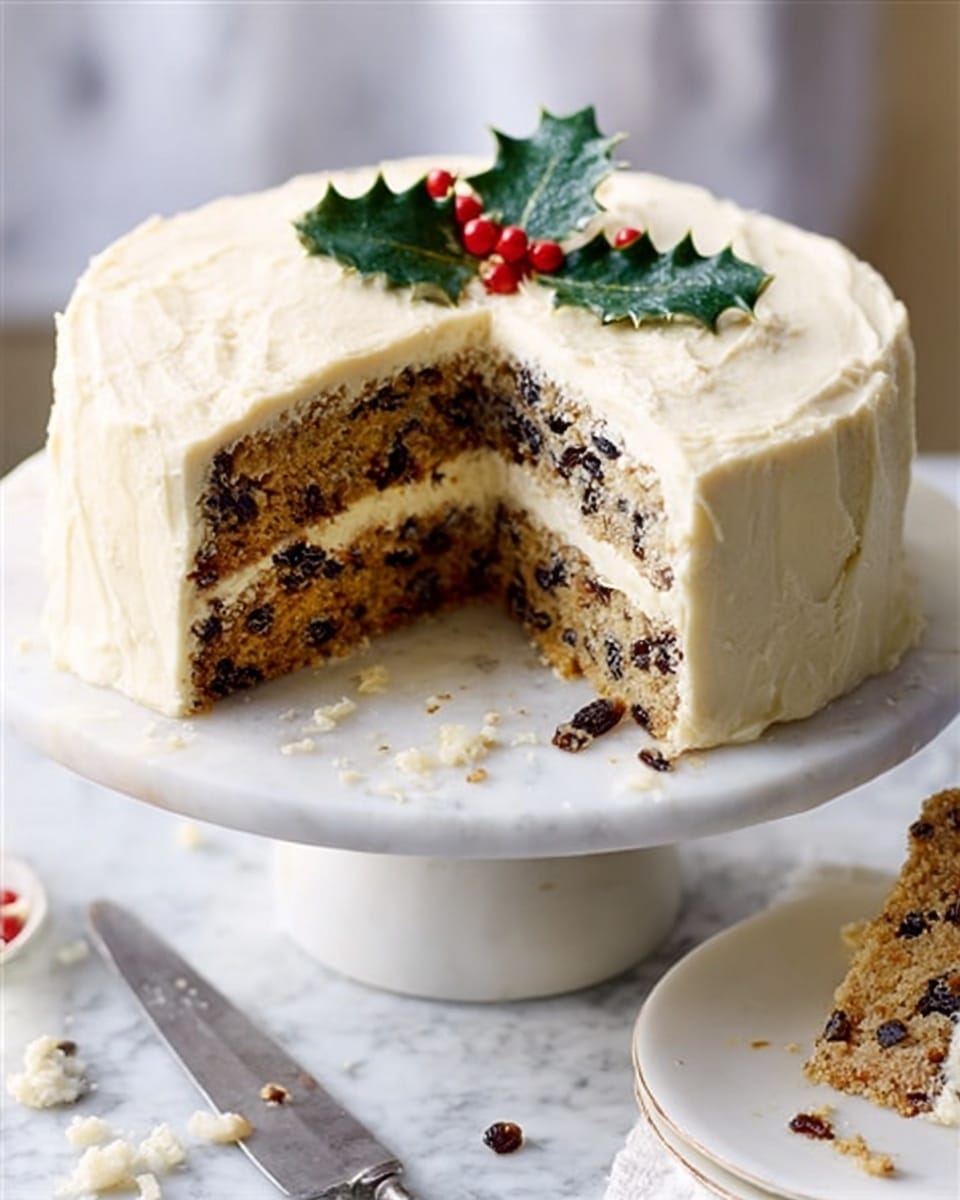 A round cake standing on a white cake stand with a textured edge, showing one slice removed to reveal the inside; the cake has two layers covered fully in creamy off-white frosting with a slightly rough texture, while the inside is packed with dark dried fruits and light brown cake crumb, topped with a sprig of green holly leaves and red berries for decoration. The background is a white marbled surface with a knife beside the cake and some cookies in the front right. Photo taken with an iphone --ar 4:5 --v 7