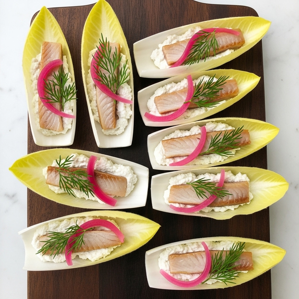 The image shows nine small appetizer boats made from pale yellow to white endive leaves arranged neatly in three rows on a wooden cutting board. Each endive leaf holds a creamy white base layer topped with a small piece of light pinkish-orange smoked salmon and a curled strip of bright pink pickled onion. A small sprig of fresh green dill rests on top of each boat, adding texture and color contrast. The wooden cutting board sits on a white marbled surface. photo taken with an iphone --ar 4:5 --v 7
