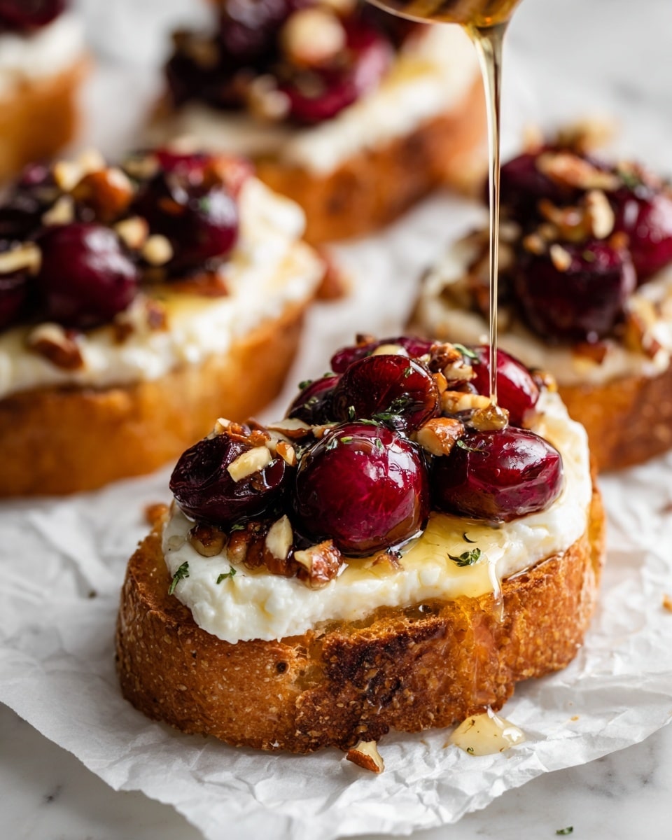 The image shows several small toasted baguette slices placed on a white marbled surface, each topped with a thick, creamy white slice of cheese. Above the cheese, bright red roasted cherries or grapes are piled, giving a vibrant contrast. Small bits of crushed nuts are sprinkled on top of the fruit, adding texture. Honey is being poured over one slice, creating a shiny, golden drizzle over the fruit and cheese. The slices have a golden-brown crust and a soft inside, making layers of crispy bread, smooth cheese, sticky honey, and juicy fruit visible. Photo taken with an iphone --ar 4:5 --v 7