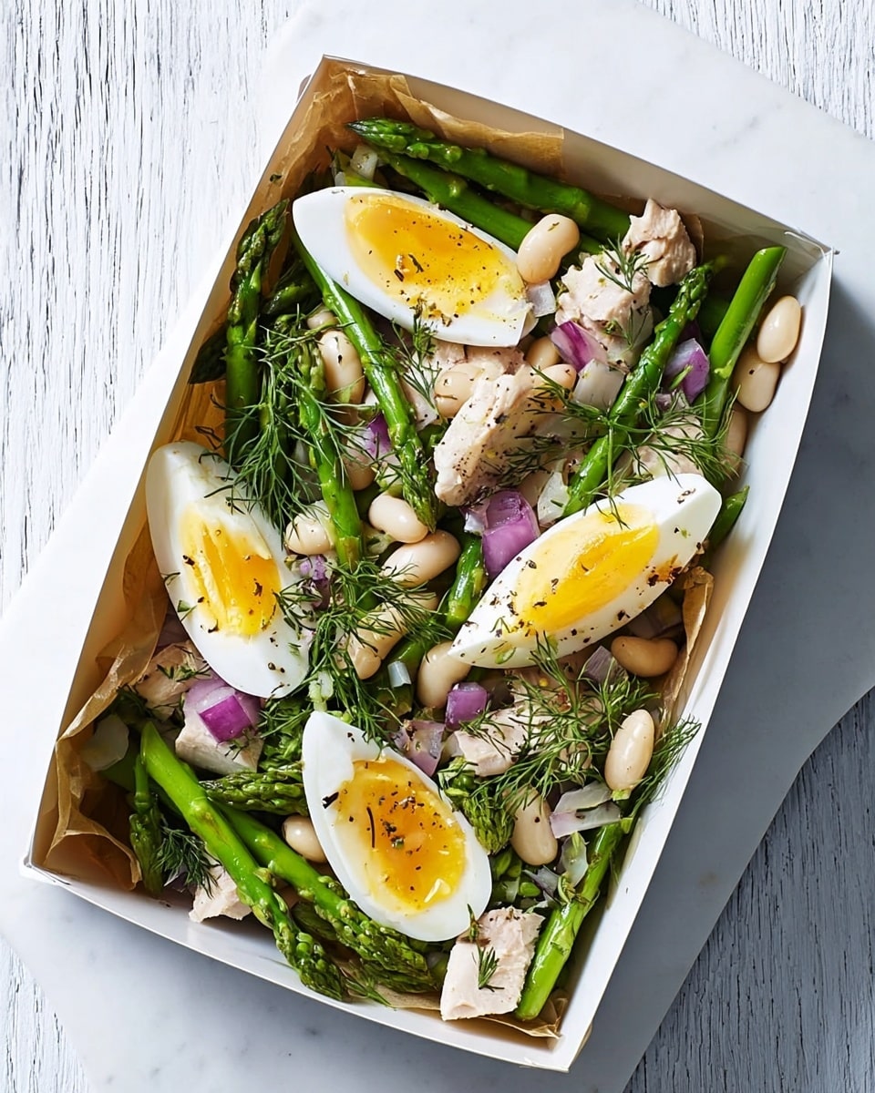 The image shows a white rectangular box filled with a fresh salad. The bottom layer contains white beans mixed with small pieces of purple onion and bits of light pink meat. On top of this are three halves of soft-boiled eggs with bright yellow yolks and white edges, garnished with small green dill sprigs and black pepper. Alongside the eggs, several thick, green asparagus stalks are laid diagonally on the right side. The box rests on a white marbled surface with a wooden fork placed at the bottom right corner. Photo taken with an iphone --ar 4:5 --v 7