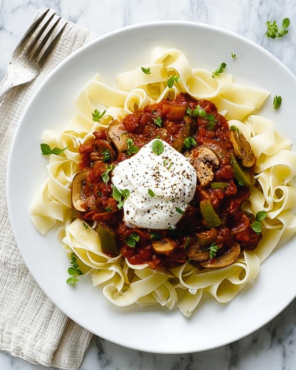 The image shows a white plate with three main layers: the bottom layer is wide, flat pasta noodles arranged loosely in a circular pattern with a creamy off-white color and smooth texture; the middle layer is a chunky tomato-based sauce with pieces of mushrooms and vegetables, rich red and brown shades, spread unevenly over the pasta; the top layer is a dollop of white cream or cheese with black pepper sprinkled on it and a few green herb leaves for garnish, sitting right in the center. The plate is placed on a white marbled surface with a fork and knife beside it. Photo taken with an iphone --ar 4:5 --v 7