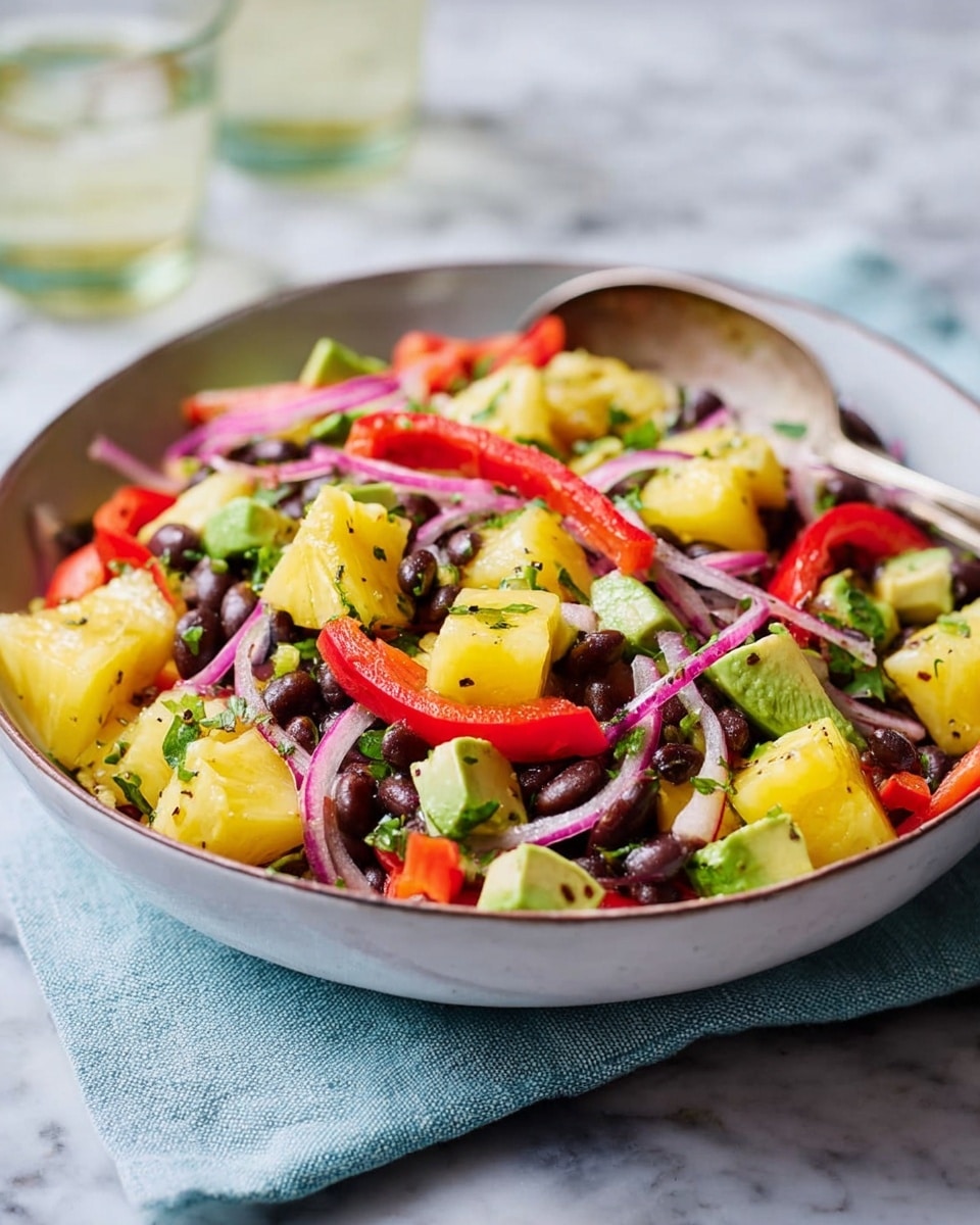 A bowl of fresh salad with three main layers: the bottom layer is a mix of dark brown beans, the middle layer shows bright yellow pineapple chunks, and the top layer has thin slices of purple onion and red bell pepper strips, garnished with small green cilantro leaves scattered throughout. The bowl is white, placed on a light gray textured cloth with a blurred white marbled surface in the background, and a silver spoon rests inside the bowl. Photo taken with an iphone --ar 4:5 --v 7