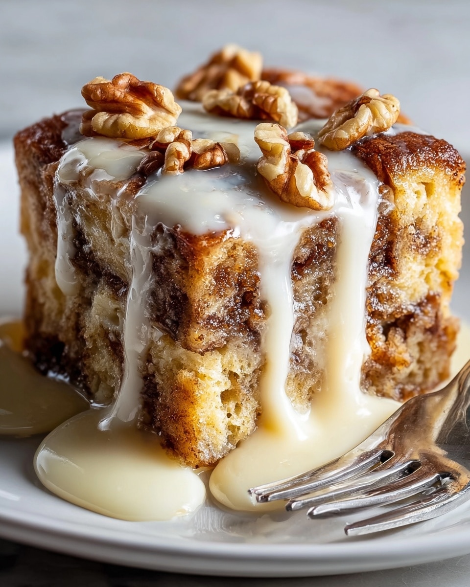 A square piece of cinnamon bread pudding sits on a white plate, showing three layers of golden brown, soft cake cubes with darker cinnamon swirls inside. Thick, white cream sauce pours down from the top, covering the upper surface and dripping over the sides in smooth streams. On top, a few walnut halves are placed as decoration. A silver fork rests gently on the plate's edge next to the pudding. The whole setting is on a white marbled surface. Photo taken with an iphone --ar 4:5 --v 7