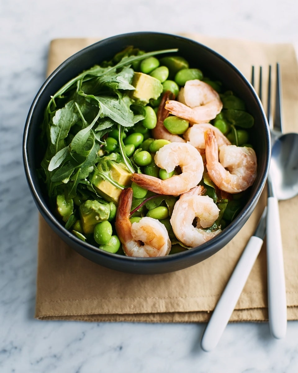 A gray bowl filled with a fresh shrimp salad rests on top of a light brown paper napkin, placed on a white marbled surface. Inside the bowl, at the bottom, there is a mix of small green edamame beans and chopped avocado with a bright green color. On top of this layer, there are whole cooked shrimp with a light pink and white color scattered evenly. The salad is finished with a layer of fresh green arugula leaves covering the shrimp and vegetables. To the right side of the bowl, there is a white fork and spoon resting next to each other. photo taken with an iphone --ar 4:5 --v 7