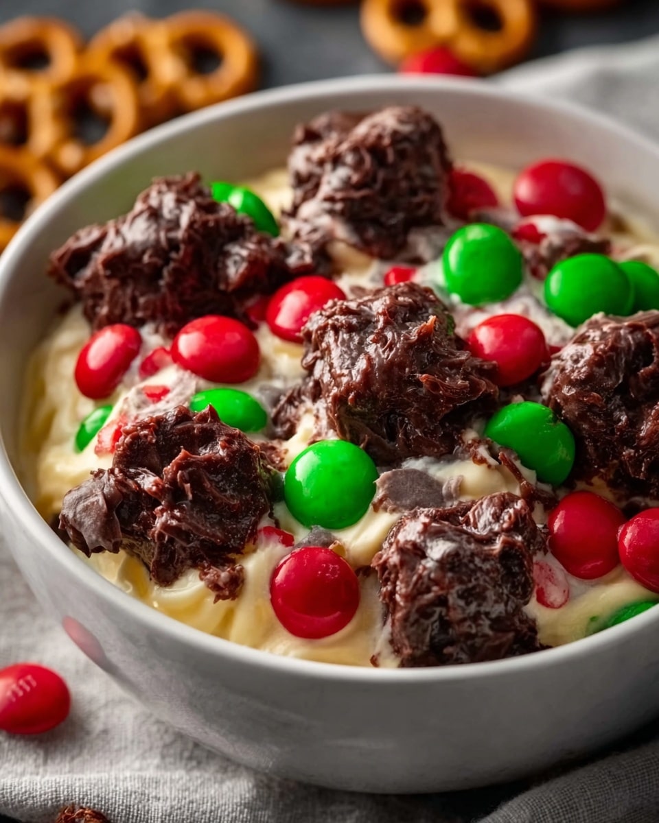 The dish shows a white bowl filled with a creamy, light tan base that looks smooth and soft. On top, there are several small clusters of melted chocolate mixed with nuts and candy-coated red and green chocolate pieces scattered evenly. The textures range from smooth and creamy at the bottom layer to chunky and rough with the chocolate and candy bits on top. The bowl sits on a white marbled surface, and a woman's hand is gently holding the bowl from one side. Photo taken with an iphone --ar 4:5 --v 7