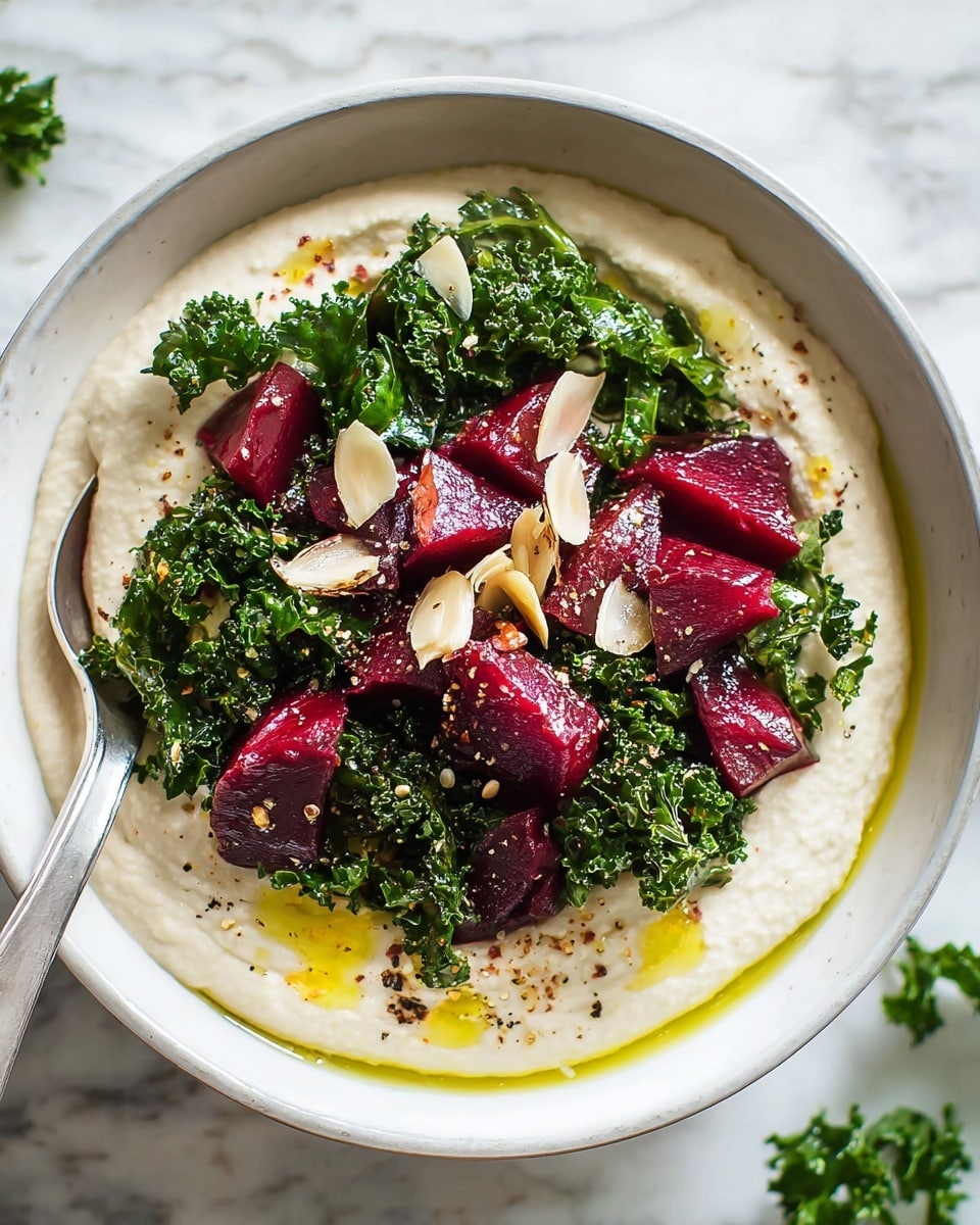 This dish is served in a white bowl, placed on a white marbled surface. It has two main layers: the bottom layer is a thick cream-colored puree with a smooth, slightly swirled texture, spread evenly across the bowl. On top, there is a pile of bright green cooked kale that looks fresh and slightly wilted. Scattered among the kale are deep red, cubed pieces of beetroot, which have a juicy, slightly glossy look. Thin, golden-brown slices of garlic are also sprinkled on top, along with a drizzle of olive oil around the edges and some cracked black pepper. The overall look is fresh, healthy, and vibrant. photo taken with an iphone --ar 4:5 --v 7