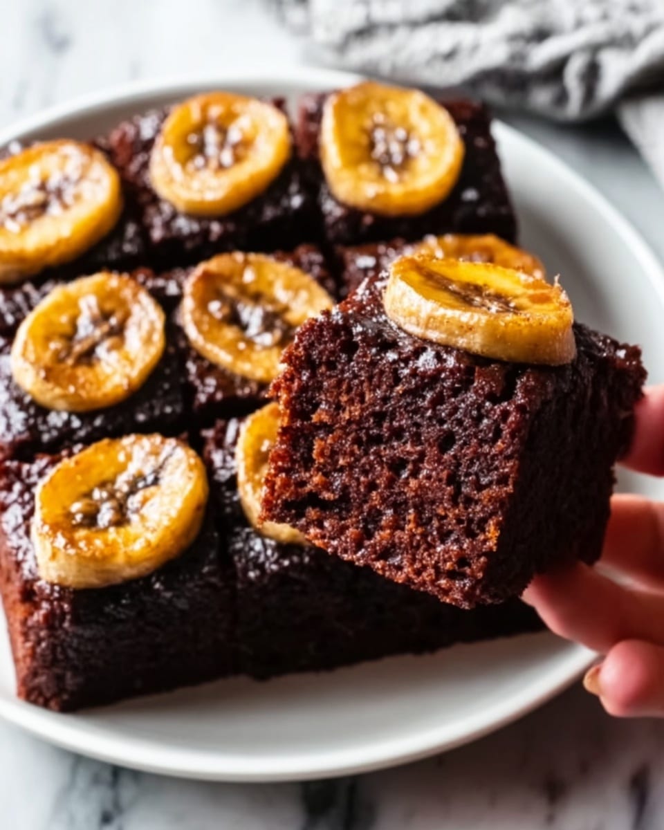 A close-up of two thick, square slices of dark chocolate cake stacked slightly on a white plate, each slice topped with shiny thin banana slices that have a caramelized look and sprinkle of light brown sugar or cinnamon, with the cake texture looking moist and rich with small crumbs visible on the surface. The background features a white marbled texture, and the photo is taken with an iphone --ar 4:5 --v 7