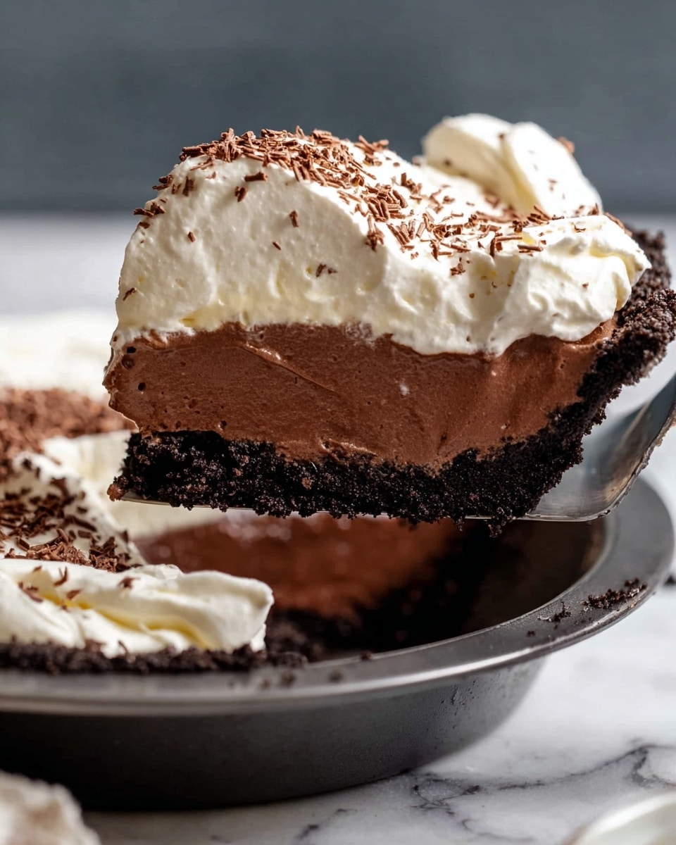 A slice of pie with three clear layers is being lifted by a metal pie server over a pie dish. The bottom crust layer is dark brown and crumbly, looking like chocolate cookie crust. The middle layer is rich, smooth, and dark chocolate colored, thick and creamy. The top layer is fluffy white whipped cream with soft swirls and sprinkled with fine shavings of dark chocolate on top. The pie dish is white, and the background has a white marbled texture. Photo taken with an iphone --ar 4:5 --v 7