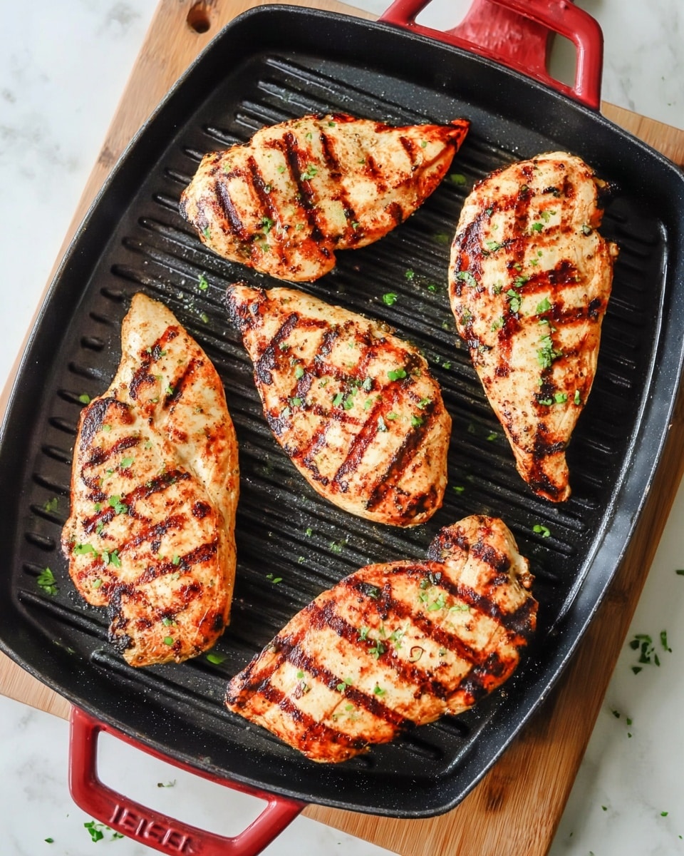 Four grilled chicken breasts with dark char grill marks and a golden-brown color are placed evenly on a black grill pan with raised ridges. Small green herb pieces are sprinkled over the chicken, adding a touch of freshness. The grill pan has red handles and is set on a wooden tray, all placed on a white marbled surface. photo taken with an iphone --ar 4:5 --v 7