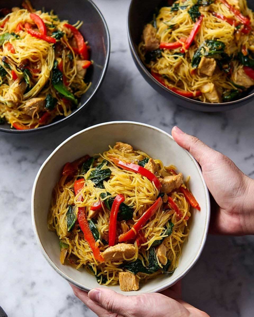 The image shows three white bowls filled with a colorful noodle dish. Each bowl has thin yellow noodles mixed with bright red bell pepper strips, leafy dark green spinach, and light golden pieces of egg or tofu scattered throughout. The textures vary from soft noodles, tender vegetables, to slightly crispy chunks. Two woman’s hands are holding and reaching into the bowls, creating a sense of sharing the meal. The bowls are placed on a white marbled textured surface with a soft grey cloth and a pair of chopsticks lying nearby. Photo taken with an iphone --ar 4:5 --v 7