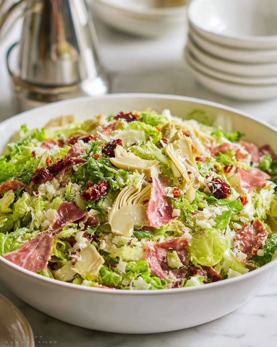 A close-up of a mixed salad served in a deep white bowl on a white marbled surface, showing multiple layers of ingredients: the base layer is light and dark green chopped lettuce with a fresh, crisp texture; interspersed throughout are small pale artichoke hearts with a soft texture positioned near the top; thin red strips of what looks like salami or similar meat add a reddish color contrast spread evenly; small bits of white cheese are scattered over the salad, adding a crumbly texture; there are also small pieces of sun-dried tomatoes with a dark red and wrinkled texture. Photo taken with an iphone --ar 4:5 --v 7