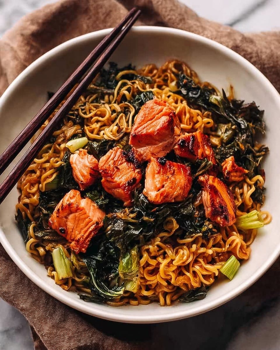 A white bowl filled with cooked ramen noodles mixed with dark green leafy vegetables scattered throughout, topped with several pieces of lightly grilled salmon showing crispy orangish-pink surfaces; the noodles have a brownish sauce coating giving a shiny texture. Dark chopsticks rest on the rim of the bowl. The bowl sits on a dark fabric over a surface with a white marbled texture. photo taken with an iphone --ar 4:5 --v 7