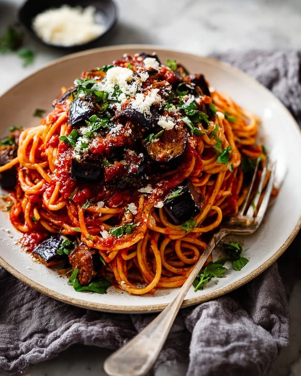 A round white plate holds a serving of spaghetti mixed with chunky red tomato sauce. There are dark brown to almost black pieces of cooked eggplant scattered throughout the pasta. The spaghetti is coated evenly in the sauce, with some strands lightly twisted on top. Fresh chopped green herbs are sprinkled over the top, adding bright color. Light beige grated cheese is dusted in the center and around the dish. A silver fork partially twirls some spaghetti on the right side of the plate. The plate rests on a white marbled surface with a soft gray cloth partially tucked underneath, and a small bowl with more grated cheese is placed nearby. Photo taken with an iphone --ar 4:5 --v 7