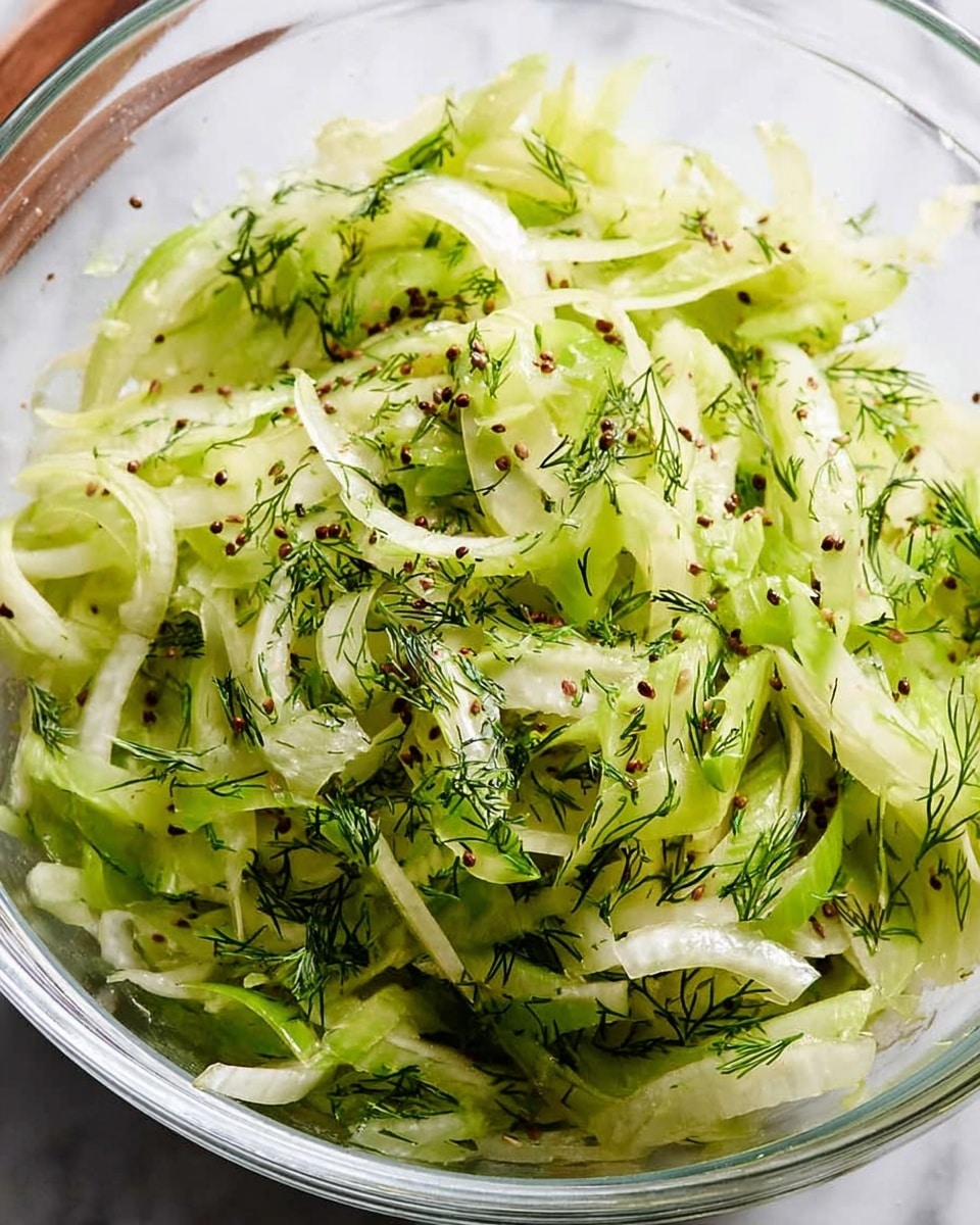 A close-up view of a fresh salad made mostly of sliced light green celery with a slightly crisp texture, mixed with thin pieces of leafy green dill and small brown caraway seeds scattered evenly throughout the pile. The salad is held in a transparent bowl with a white marbled texture background visible behind it, and a wooden spoon resting on the side, partially covered. photo taken with an iphone --ar 4:5 --v 7