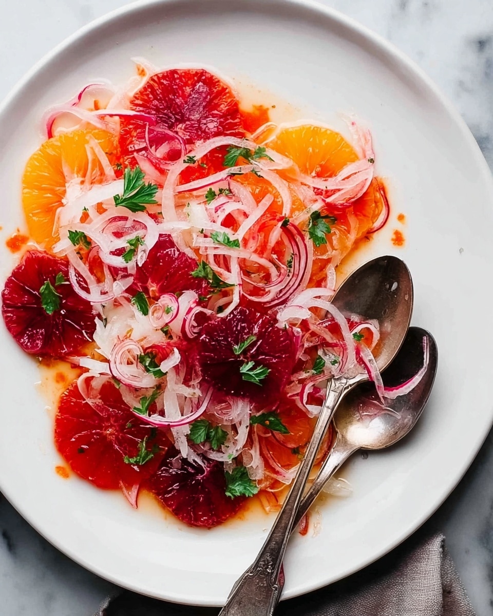 A white plate holds a salad made of three main layers: a base layer of deep red and dark maroon blood orange slices arranged in a loose circle, topped with a second layer of thin, white and slightly pinkish sliced onions placed in loose piles across the orange slices, and a final layer of fresh small green parsley leaves scattered evenly around the salad. Light orange dressing lightly coats some parts of the plate and salad, pooling slightly around the edges. Two silver spoons rest on the right side of the plate. The background is a white marbled texture. Photo taken with an iphone --ar 4:5 --v 7