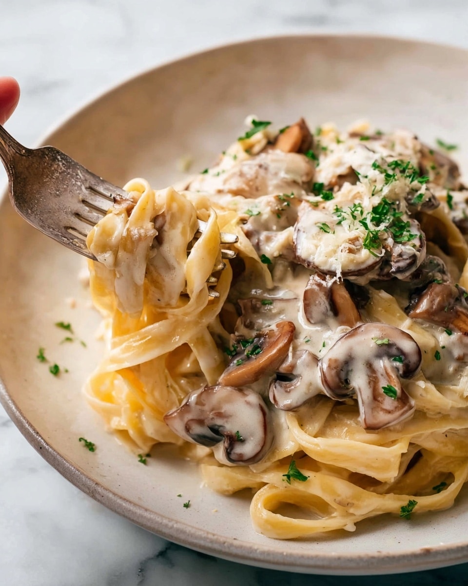 The image shows a close-up of creamy mushroom pasta served on a white plate set on a white marbled surface. The dish has two main layers: the bottom layer consists of thick, light yellow fettuccine noodles with a smooth, creamy texture, and the top layer is made of sliced, sautéed brown mushrooms coated in a rich, white cream sauce. Freshly chopped green parsley is sprinkled over the mushrooms, adding a touch of color. In the bottom left corner, a silver fork twirls some pasta and mushrooms, appearing partially embedded in the dish. Photo taken with an iphone --ar 4:5 --v 7